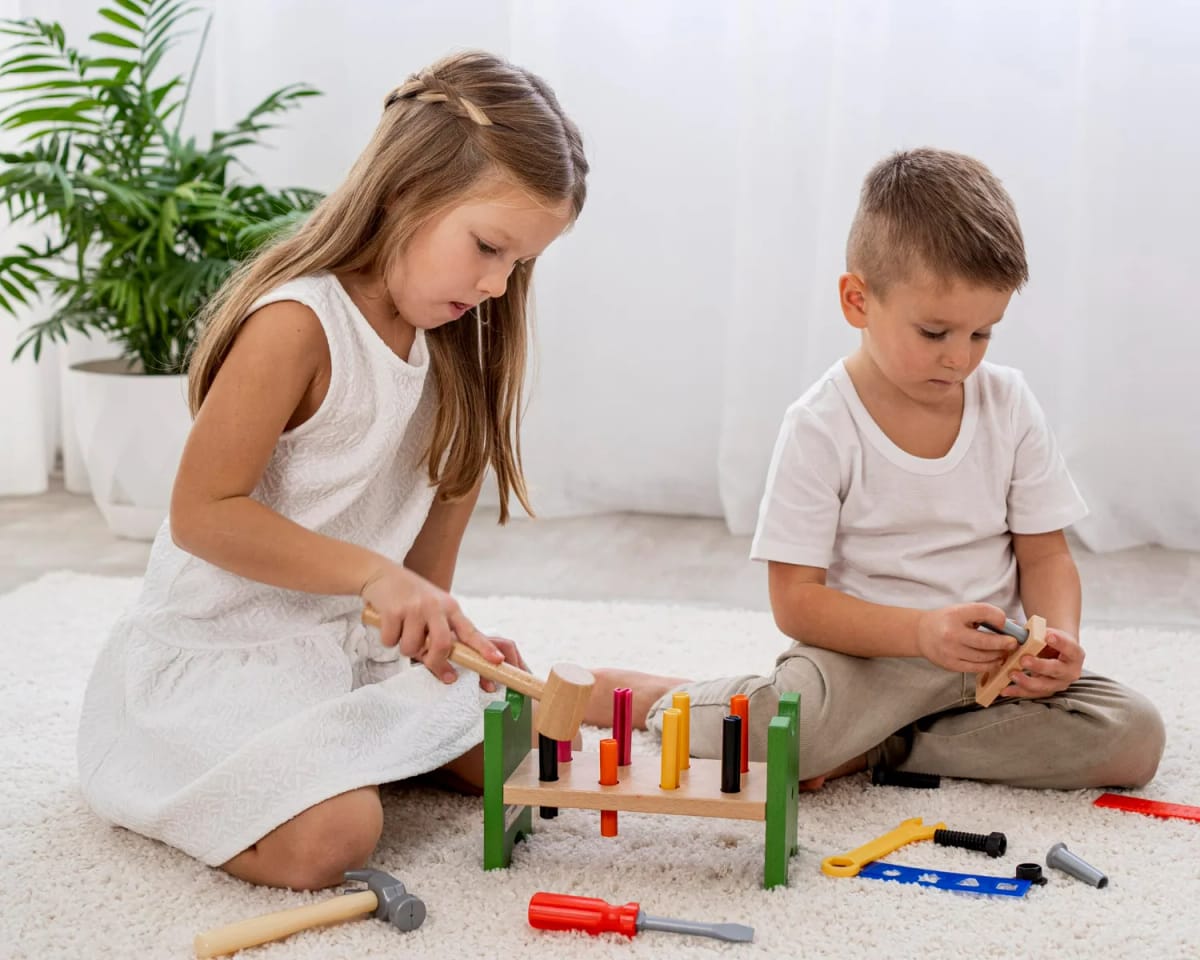 Girl and boy sitting on floor playing with toy tools and wooden peg board on a white rug.