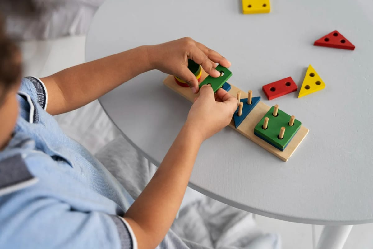 Child assembling colorful wooden shape sorting toy on a gray table.